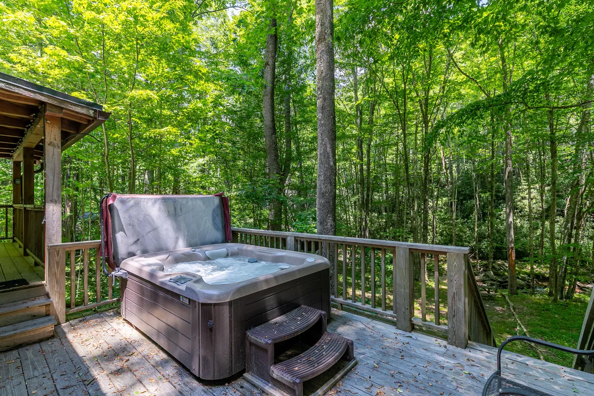A cozy view of the deck with a bubbling hot tub, surrounded by wooden planks and leafy trees. The scene conveys a sense of intimate seclusion, perfect for stargazing at night or sharing a quiet moment. The hot tub’s placement and the deck’s design seamlessly blend comfort with the beauty of the outdoors.