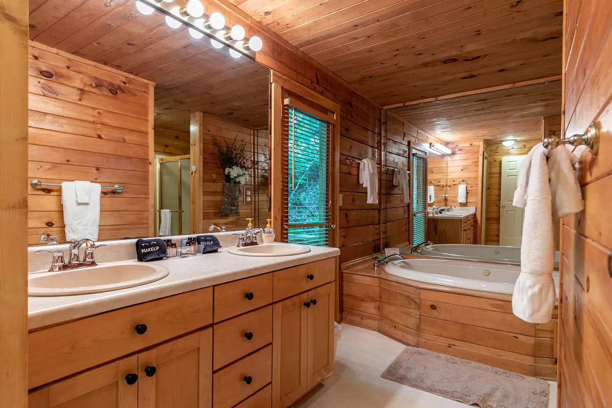 This image features a serene bathroom setting with a spacious double sink vanity, a large bathtub perfect for soaking, warm wooden cabinetry, and soft natural light filtering through the windows. The tranquil ambiance is enhanced by thoughtful design details, making the space inviting for relaxation and quiet self-care moments.