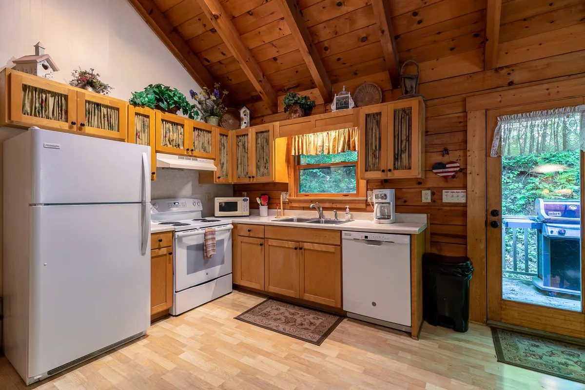 A close-up view of the kitchen area, highlighting modern appliances, warm wooden cabinets, decorative touches, and a large window framing the lush outdoors. The scene is bathed in natural light, inviting a sense of tranquility and connection to nature.